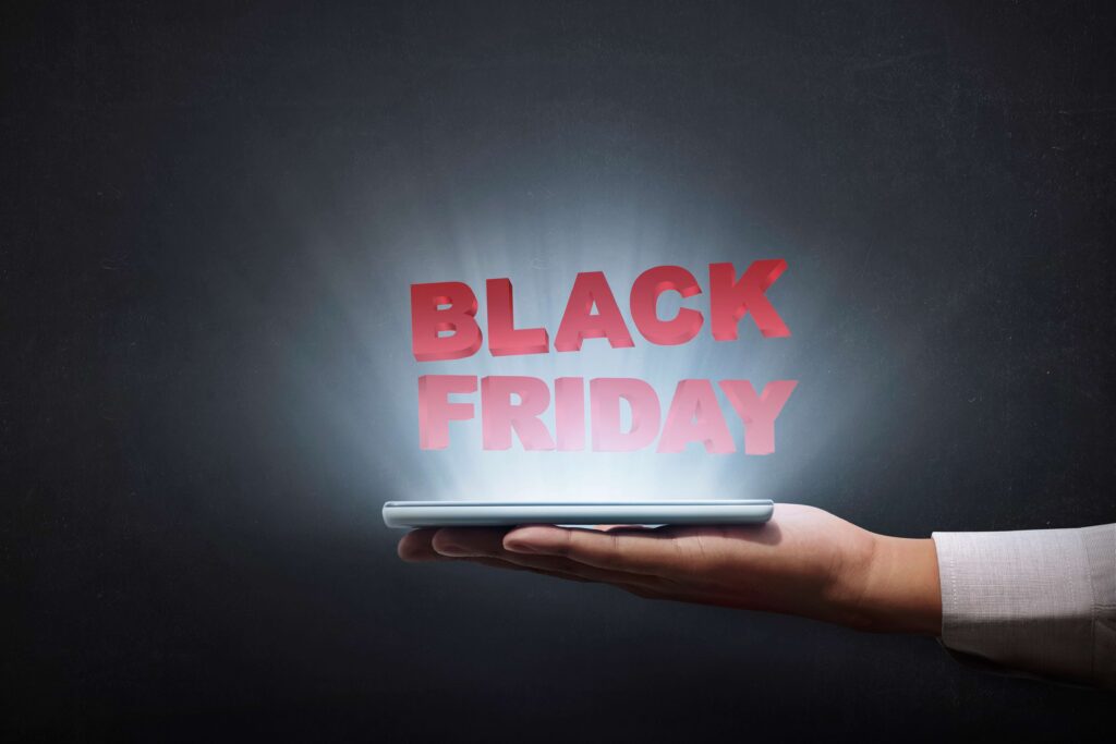 A hand holding a tablet which illuminates light and above it the heading BLACK FRIDAY in red color is floating.