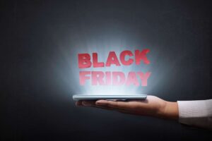 A hand holding a tablet which illuminates light and above it the heading BLACK FRIDAY in red color is floating